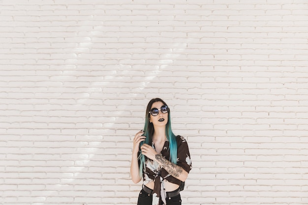 Modern young woman with tattoo on hand posing in front of wall