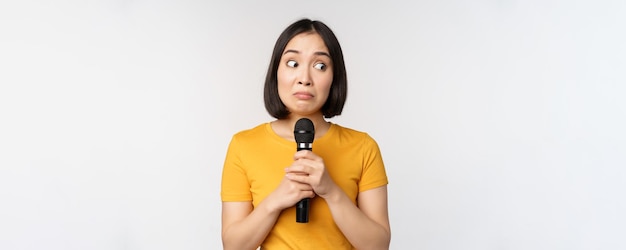 Modest asian girl holding microphone scared talking in public standing against white background Copy space