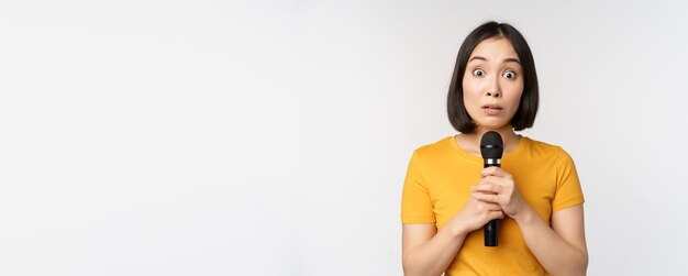 Free photo modest asian girl holding microphone scared talking in public standing against white background