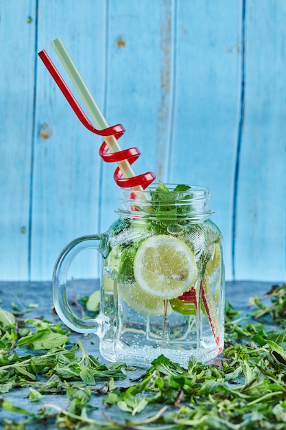 Free photo mojito cocktail with slices of lime and mint on blue table with fresh mint leaves