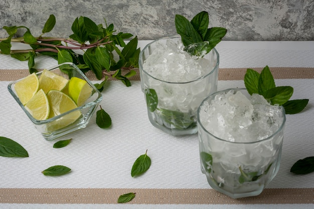 Mojito served in a crystal glass with lemon slices and mint leaves on a white table