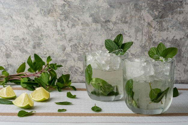 Mojito served in a crystal glass with lemon slices and mint leaves on a white table