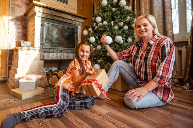 엄마와 딸 크리스마스 트리 근처에서 공을가지고 노는. 선물, 조명, 백그라운드에서 공. 프리미엄 사진