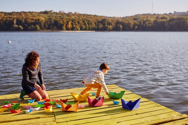 Бесплатное фото Мама и сын играют с бумажными корабликами у озера