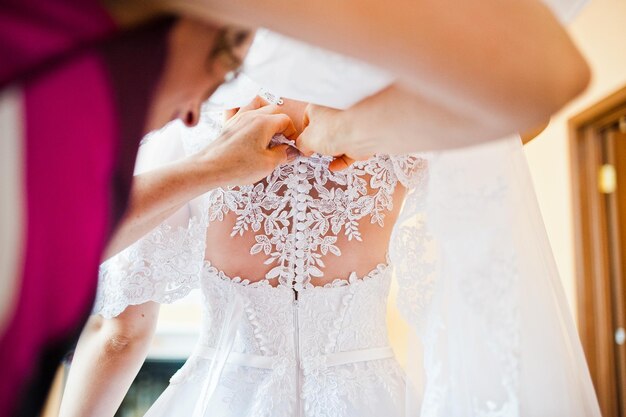 Мама застегивает пуговицы на платье невесты