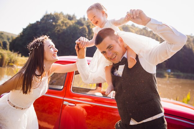 Mom and dad jump with their little daughter before a red car 