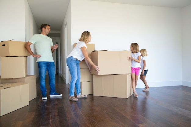 Mom, dad two girls carrying boxes and making stack in their new empty flat