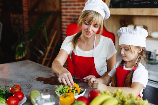 엄마와 딸이 저녁 식사를 위해 다른 야채를 요리하는 주방에서 즐거운 시간을 보내십시오.