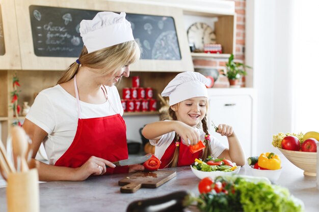 Mom and daughter have fun on the kitchen cooking different vegetables for a dinner