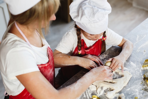 Mom and daughter have fun preparing cookies with milk at a dinner table in cosy kitchen