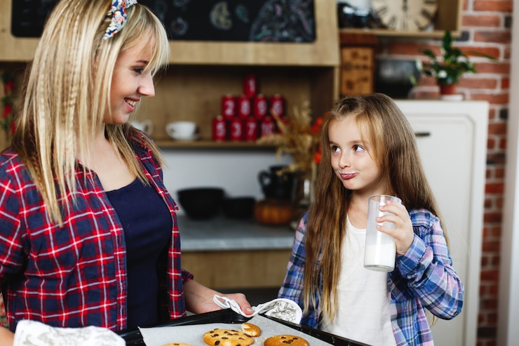 Free Photo mom and daughter on a kitchen taste together fresh baked chocolate cookies with milk