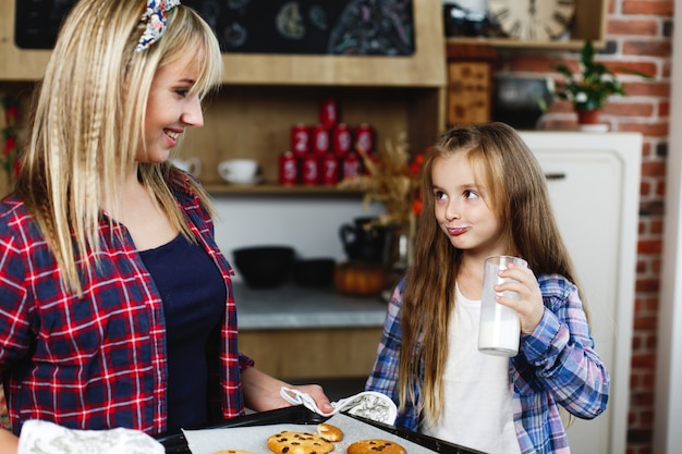 Mom and daughter on a kitchen taste together fresh baked chocolate cookies with milk