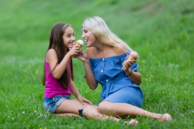 Мама и дочка в парке едят мороженое