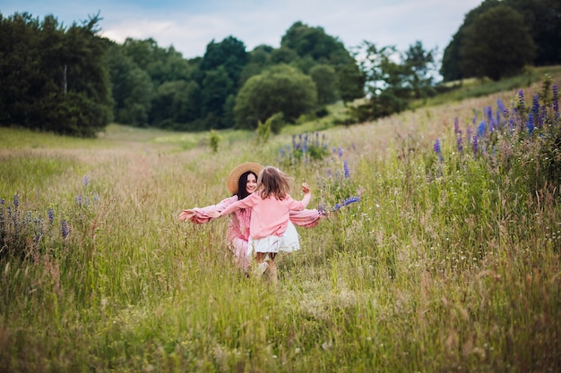Mom and daughter in pink dresses run barefooted on the field 
