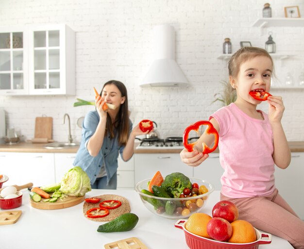 Mom and daughter prepare a salad in the kitchen. Have fun and play with vegetables