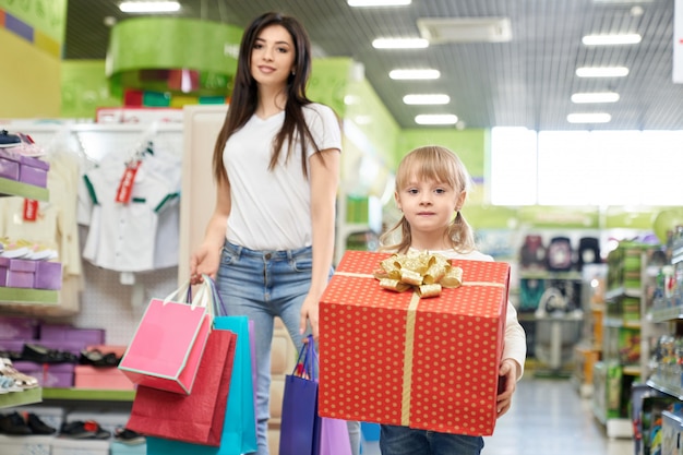Mom and daughter in store with shopping bags and present box