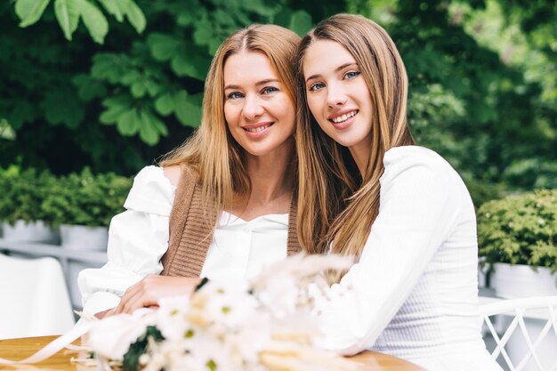 Mom and girl smiling and hugging on summer terrace in the cafe