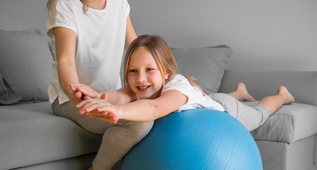 Mom helping girl to exercise on ball