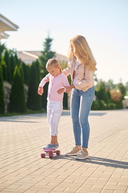 딸이 스케이트보드 타는 것을 돕는 엄마