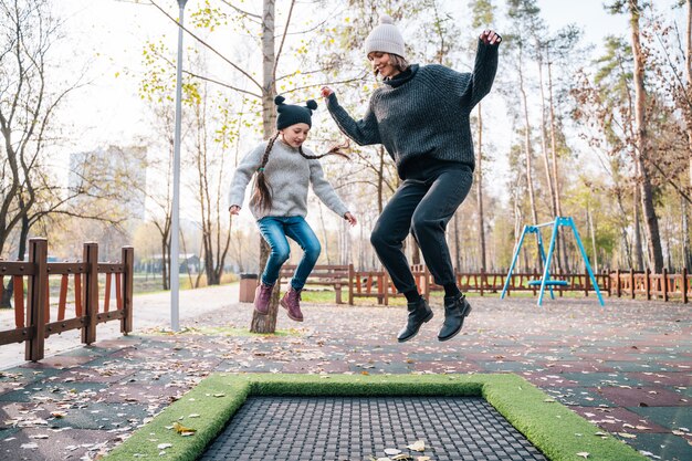 Free photo mom and her daughter jumping together on trampoline in autumn park