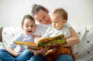 Foto gratuita la mamma ei suoi due figli stanno leggendo un libro a casa su un divano. felice e sorridente