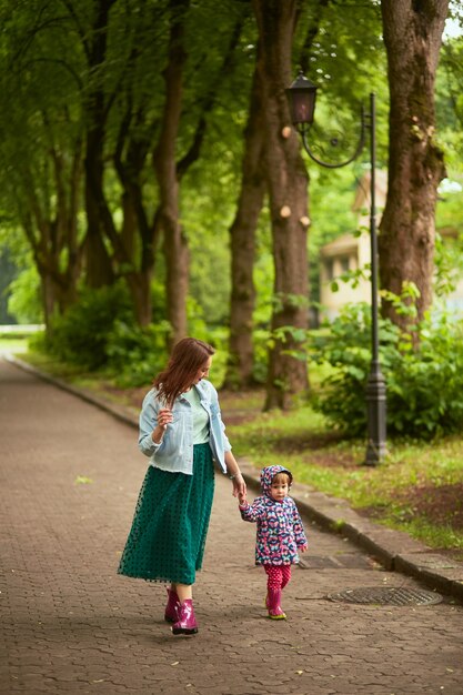 Mom holds daughter's hand walking with her in the park after rain