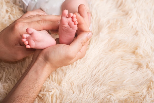 ママは小さな赤ちゃんの足を手に持っています。母親の手に生まれたばかりの赤ちゃんの小さな足。ベビーフットマッサージ