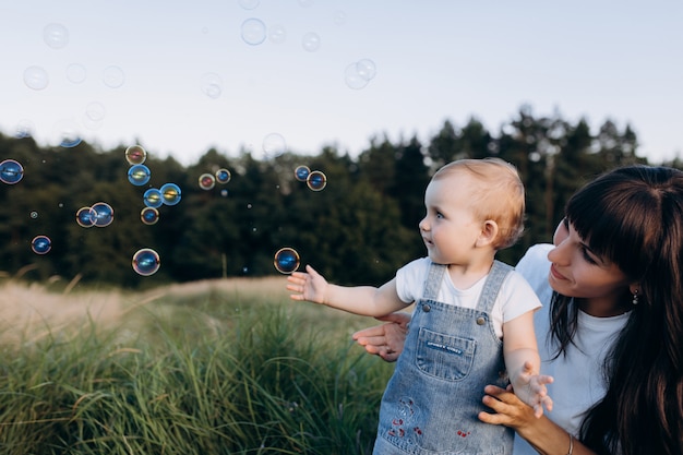 Free photo mom holds little daughter on her arms while soap balloons fly around them