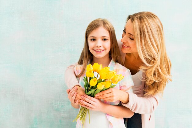 Mom hugging daughter with tulips and looking at girl