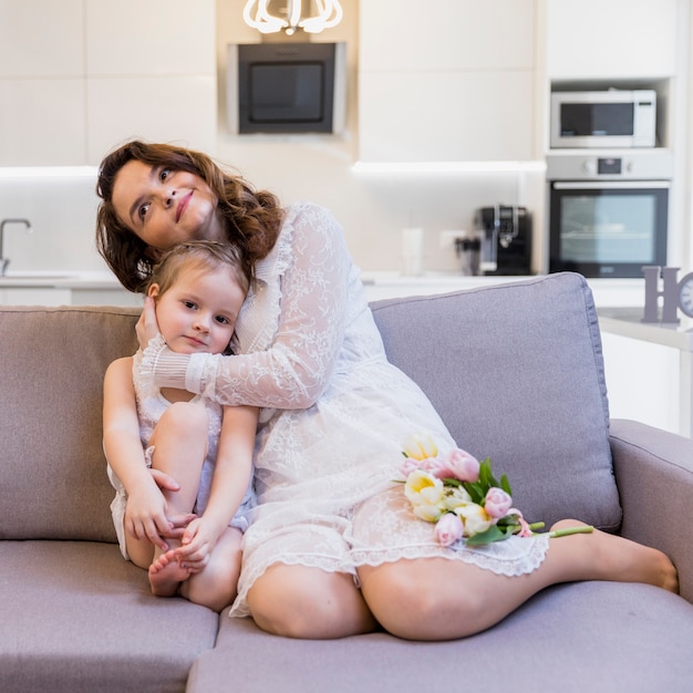 Mom hugging her child girl sitting on sofa