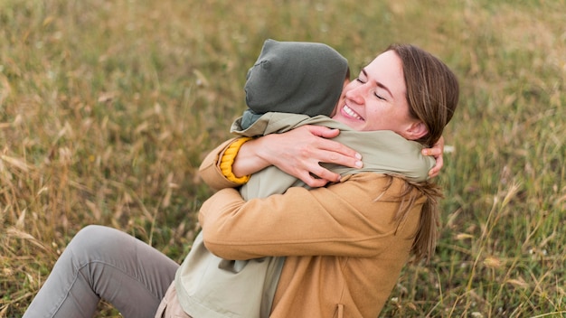 Foto gratuita mamma che abbraccia suo figlio mentre era seduto sull'erba