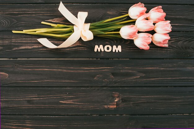 Mom inscription with tulips bouquet on dark table