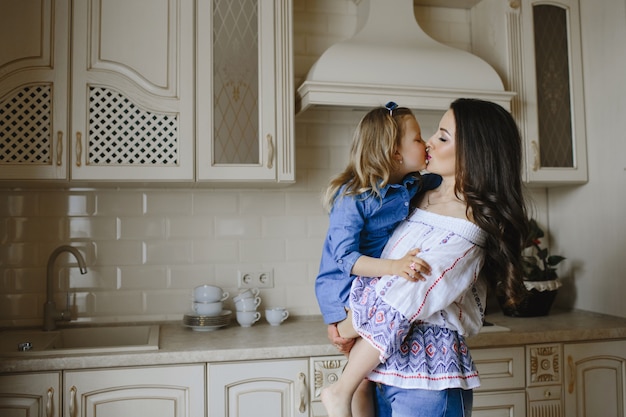 mom kisses a little daughter in the kitchen