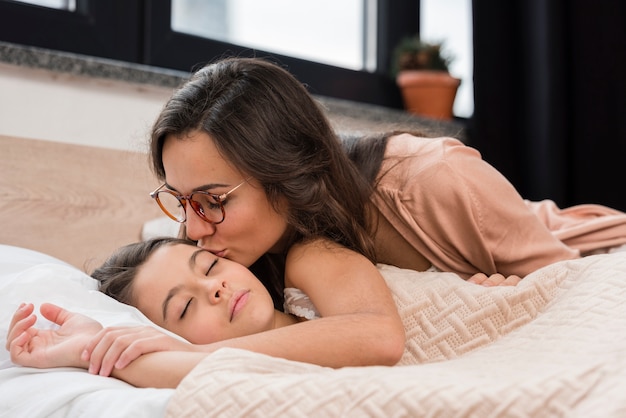 Mom kissing her daughter goodnight