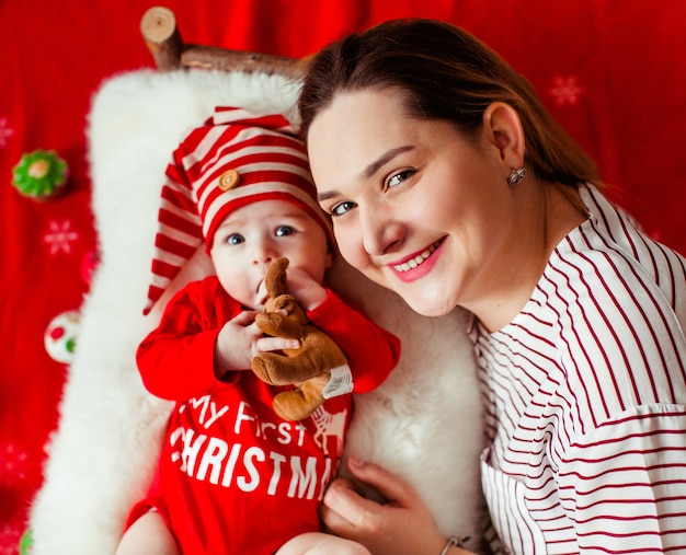 Free photo mom lies before her funny daughter in a red suit with lettering 'my first christmas'