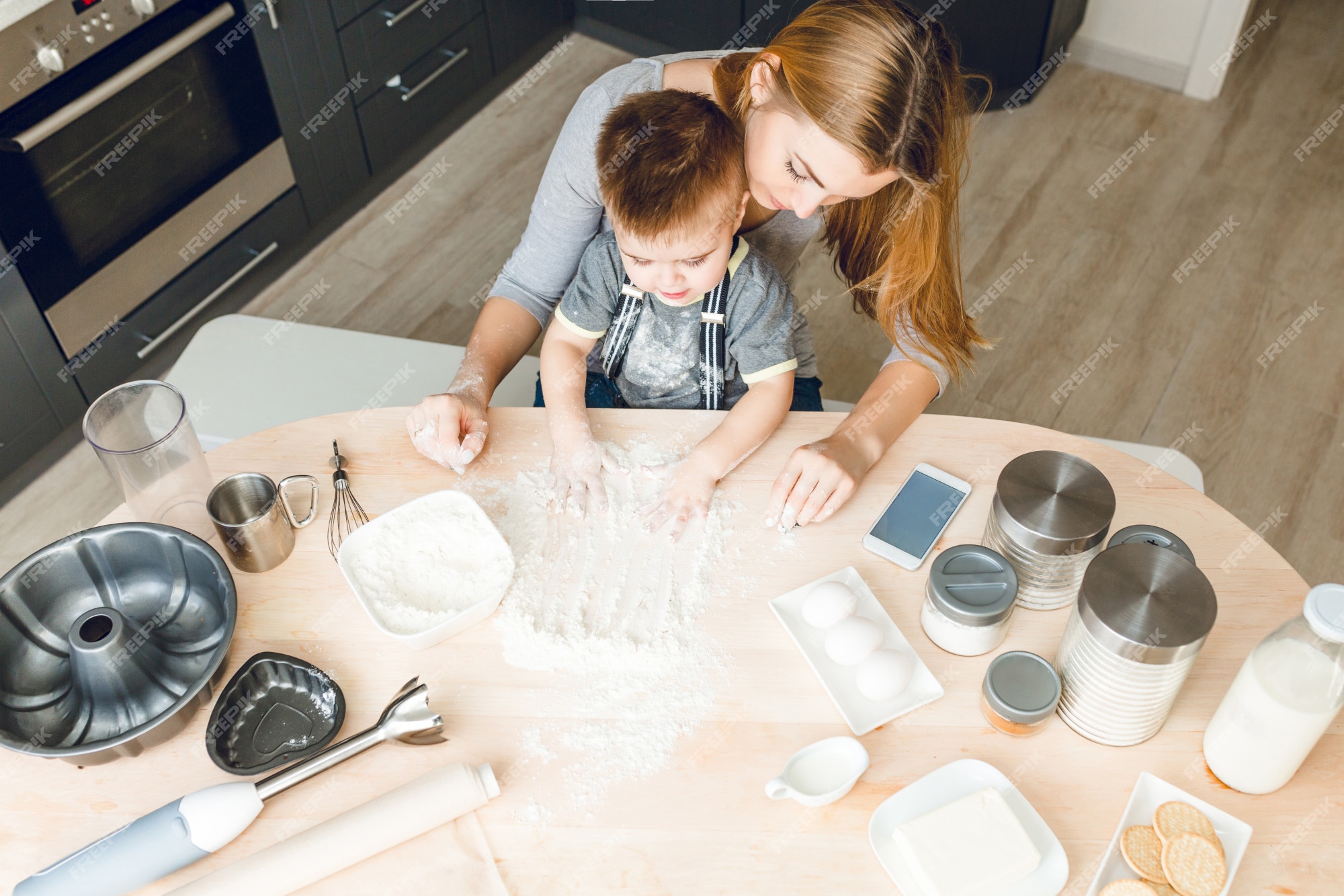 Free Photo  Mom and son sitting behind kitchen table with kitchen stuff on  it