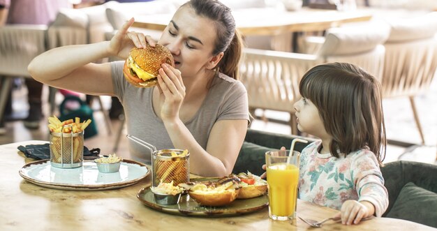 Mom with a cute daughter eating fast food in a cafe