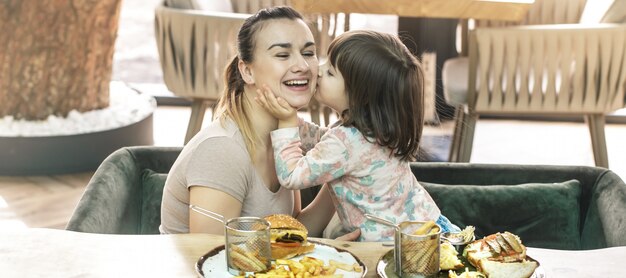 Mom with a cute daughter eating fast food in a cafe