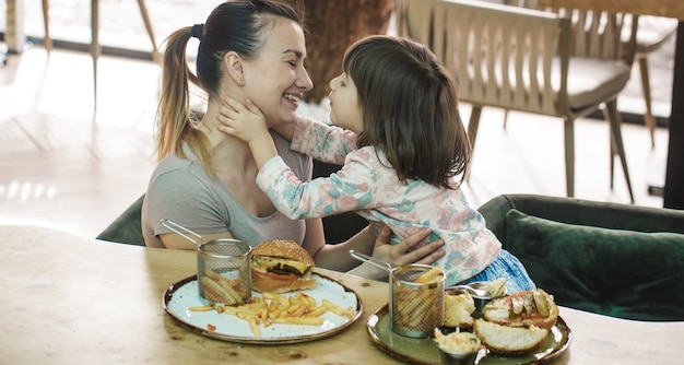 Mom with a cute daughter eating fast food in a cafe