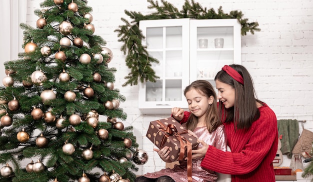 Mamma con una figlia piccola vicino all'albero di natale con una confezione regalo