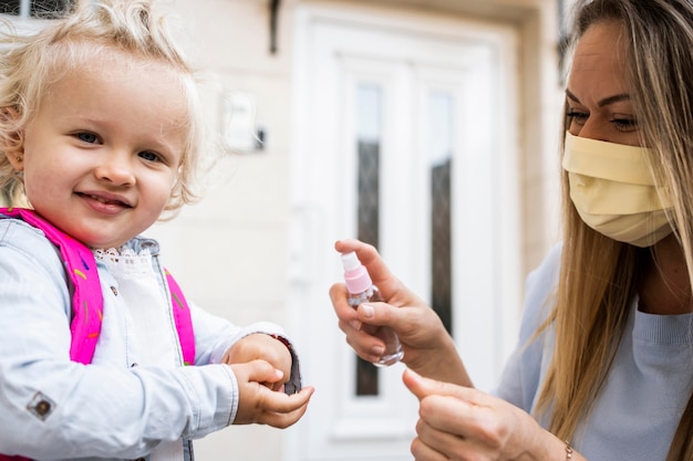 Mom with medical mask spraying child's hands with sanitizer