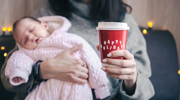 Mom with a newborn girl holding a glass of coffee happy holidays concept