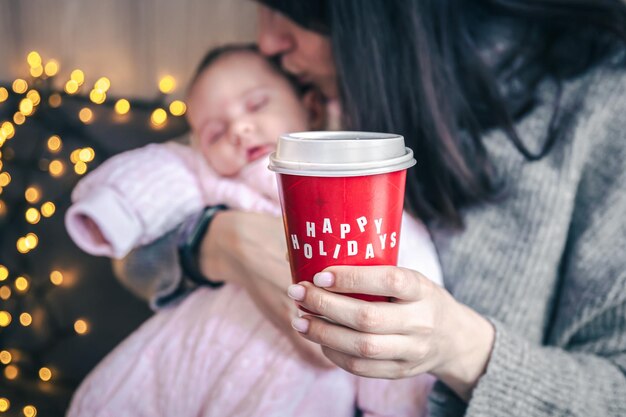 Mom with a newborn girl holding a glass of coffee happy holidays concept