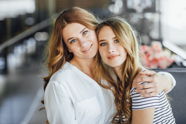Mom and young beautiful teenage daughter hug on a summer terrace cafe in casual clothing