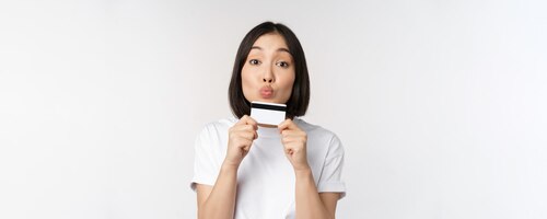 money and finance concept cute japanese girl kissing her credit card standing in tshirt over white background