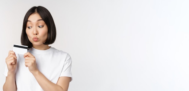 Концепция денег и финансов милая японская девушка целует свою кредитную карту, стоящую в футболке над белым б