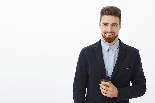 Money likes confidence. Self-assured charismatic and intelligent handsome man with brown hair, beard and blue eyes holding paper cup of coffee smiling happily meeting cute girl after work in cafe