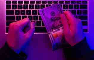 Free photo money in male hands on the background of a laptop keyboard in neon lighting