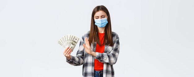 Free photo money transfer investment covid19 pandemic and working from home concept displeased girl in medical mask rejecting taking cash as bribe show stop sign to dollars and frowning bothered