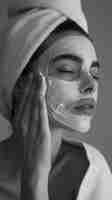 Free photo monochrome portrait of woman applying skincare